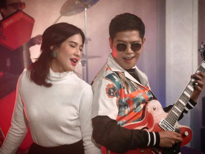 Dian Sastro memakai Turtleneck putih berdiri di sebelah Nino RAN yang memakai kacamata hitam dalam cuplikan video Serenata Jiwa Lara.